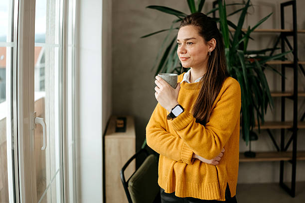 istock Woman is standing by the window and drinking coffee 2209325455