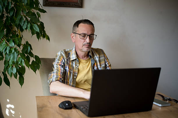 istock Mature man working on laptop while sitting at dining table at home 2209331297