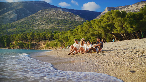 Diverse Couples Relaxing on Zlatni Rat Beach at Sunset with Serene Mountain Backdrop
