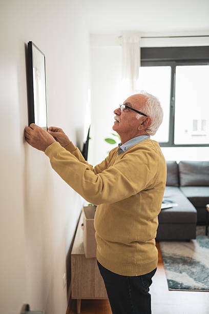 istock Senior man adjusting picture frame on wall in home interior 2209337162