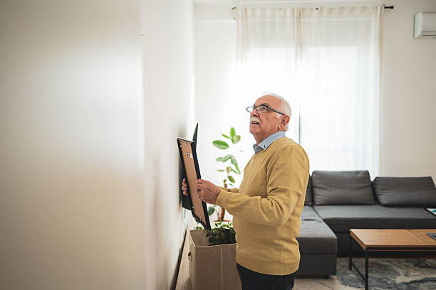 istock Senior man adjusting picture frame on wall in home interior 2209337172