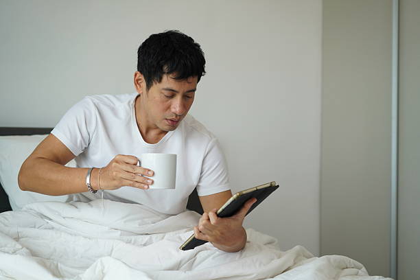istock Man reading tablet and drinking coffee in bed 2209337408