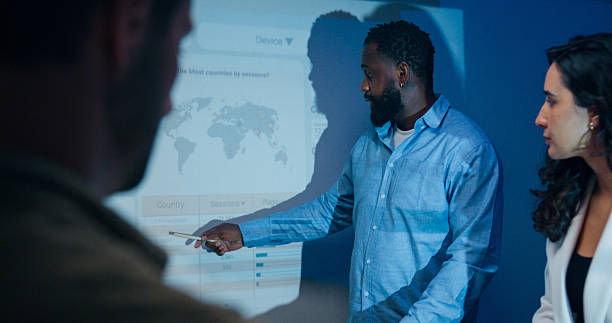 istock Group of businesspeople working late analyzing financial data displayed on projection screen while discussing strategy and planning for future business growth at office night. Finance meeting. 2209349469