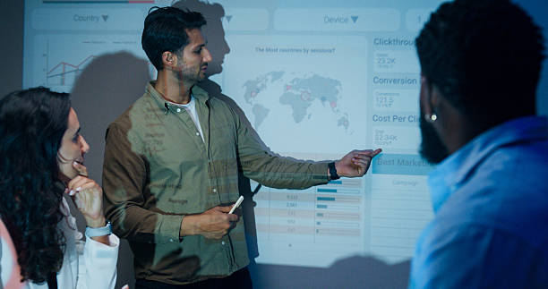 istock Group of businesspeople working late analyzing financial data displayed on projection screen while discussing strategy and planning for future business growth at office night. Finance meeting. 2209349473