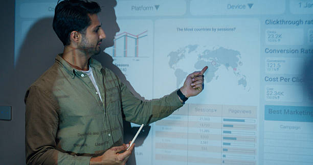 istock Group of businesspeople working late analyzing financial data displayed on projection screen while discussing strategy and planning for future business growth at office night. Finance meeting. 2209349494