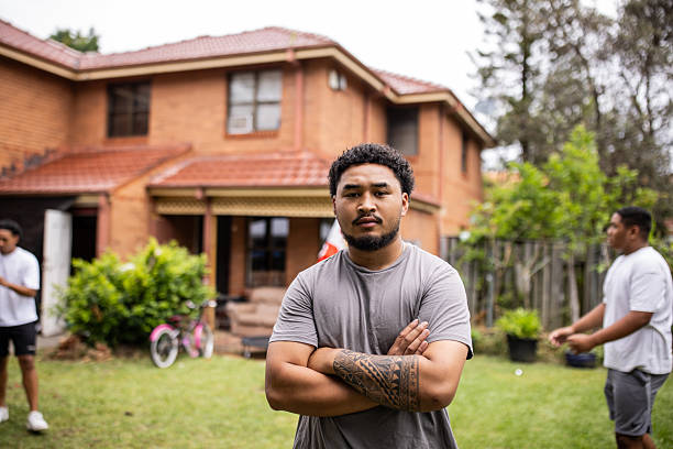 Handsome Tongan man with a visible tattoo stands confidently in the foreground, while his brothers share a moment in the background. A powerful display of sibling connection and cultural identity.