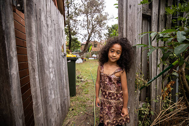 Portrait of a sweet young girl stands near a wooden fence in the backyard, taking in her surroundings.