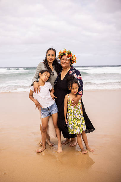 Pacific Islander mother and her three children stand together in the soft sand, enjoying the calm waves and the beauty of the ocean.