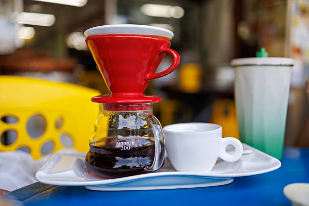 A pour-over coffee brewing set with a red dripper and glass carafe served with a white cup at an outdoor table of a local cafe.