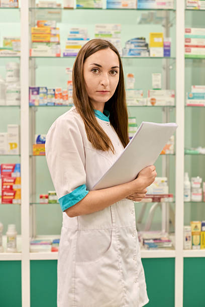 istock Young female pharmacist holding documents in bright pharmacy room 2209368026
