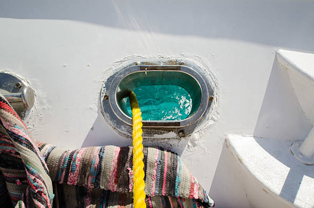 Bright yellow rope dangles into serene turquoise waters of Red Sea, framed by boats gleaming structure. Sunlight casts playful shadows, highlighting nautical details against stark white background