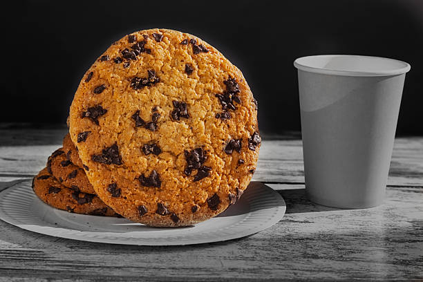 istock A lonely cookie on a black-and-white background next to a disposable coffee cup as a symbol of a small treat. Represents a light sweet snack. Cookie with chocolate chips on a white plate. 2209368416