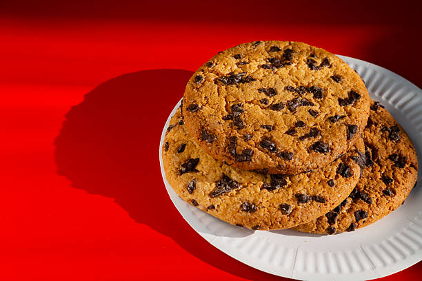 istock A large homemade chocolate cookie on a white disposable plate in bright sunlight, resting on a red table. A warm atmosphere of home comfort and enjoyment of taste. 2209368424