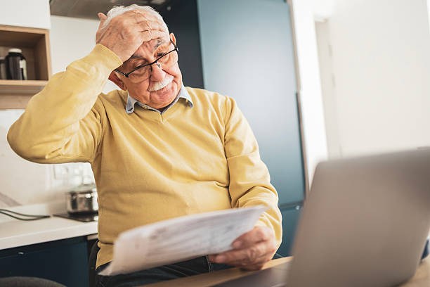 istock Senior man struggling with bills while using a laptop at home 2209370642