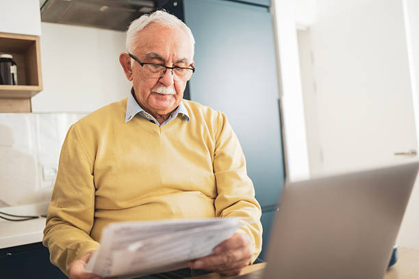 istock Senior man reading a document at home wearing a yellow sweater 2209370644