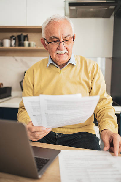 istock Senior man reviewing documents at home with a laptop and thoughtful expression 2209370645