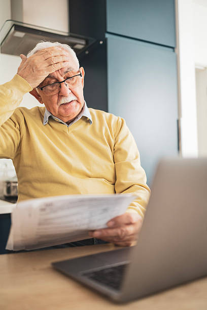 Senior man struggling with bills while using a laptop at home