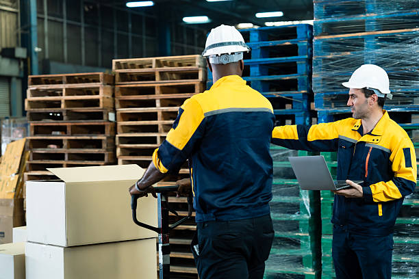 istock Warehouse teamwork with male logistics workers wearing uniform and helmet managing cardboard boxes and giving direction during material handling process in distribution center 2209371488