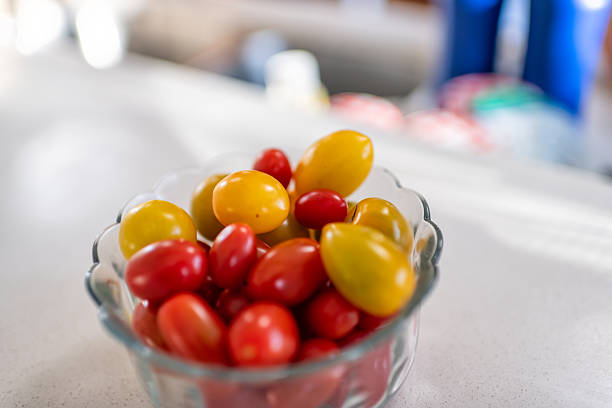 Cherry tomato small vegetable fruit of red yellow color in glass bowl plate, healthy snack macro closeup on kitchen room table