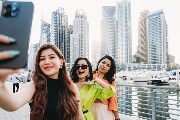 Three young women capturing a joyful selfie with the stunning Dubai Marina skyline and luxurious yachts in the background