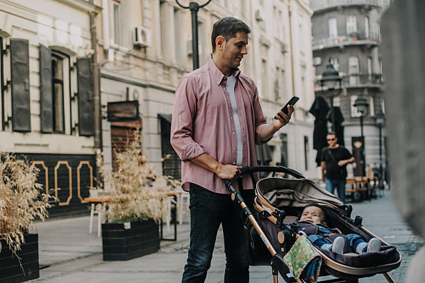 istock Father with Baby Stroller Using Smartphone in City Street 2209382736