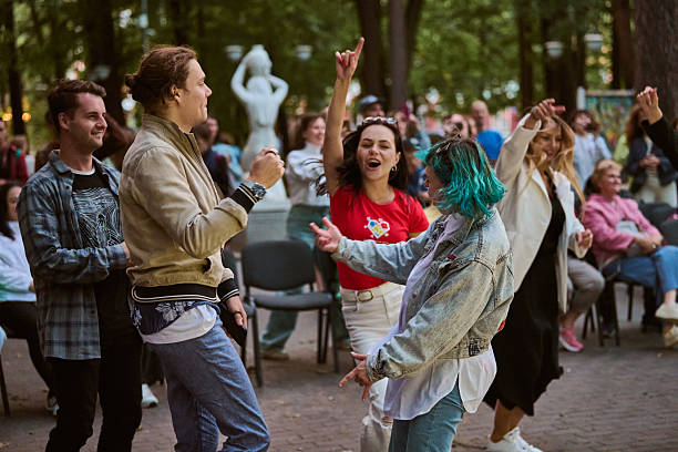Kaliningrad, Russia - 11.08.2024 - Young adults dance energetically in park setting. Diverse group, joyful expressions. Greenery and statue in background