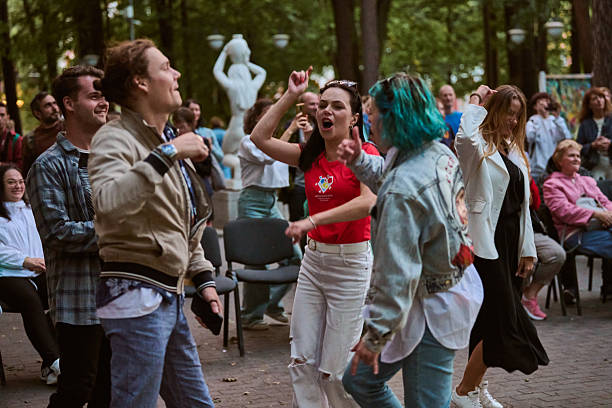 Kaliningrad, Russia - 11.08.2024 - Young adults of diverse ethnicities dance energetically in lively park scene. Overcast day, with statues and trees in background