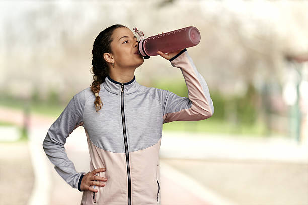 Young athletic fitness woman in sportswear holding bottle with vitamins, capsules or pills and looking at camera while standing isolated over beige background. Healthy lifestyle and sport