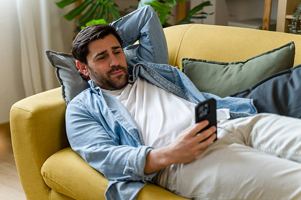 istock Young man relaxing on sofa using mobile phone at home 2209395400