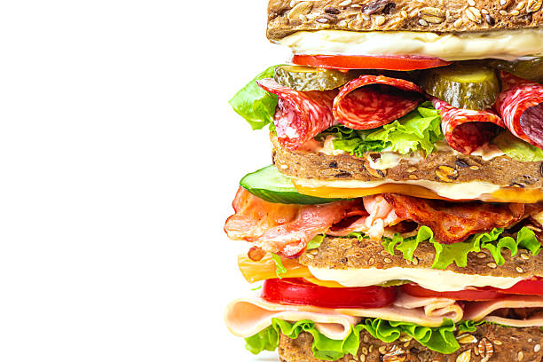 Layered mega sandwich with ham, bacon, salami, cheese and fresh vegetables isolated on white background, extremely close up. Detailed healthy food design, lunch sandwich concept.