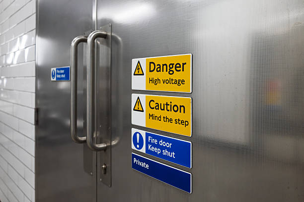 Stainless steel doors marked with high voltage and fire door safety warnings.