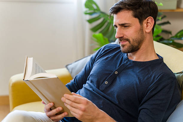 istock Man relaxing on sofa reading a book at home 2209397346