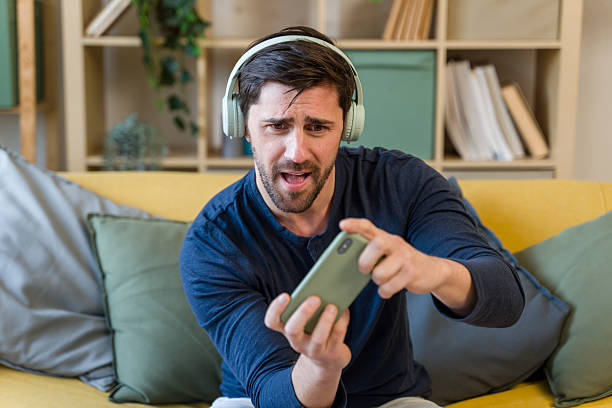 istock Excited man playing video games on smartphone at home 2209397451