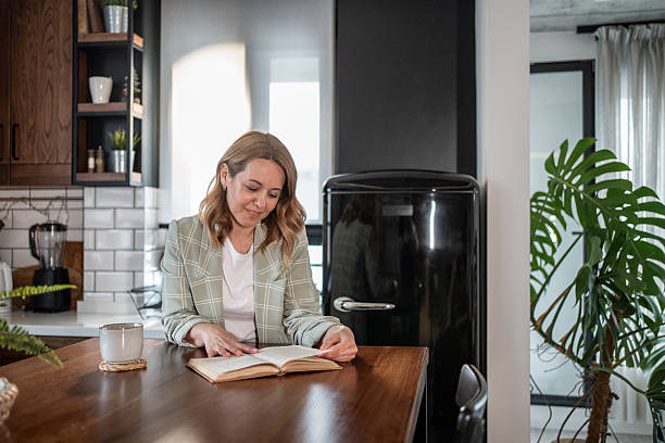istock Businesswoman reading a book in her modern kitchen during a break 2209401818
