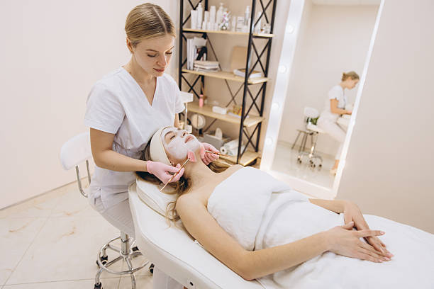 istock Cosmetologist applying a white clay mask to a client's face using rose quartz rollers in a professional beauty salon 2209401873