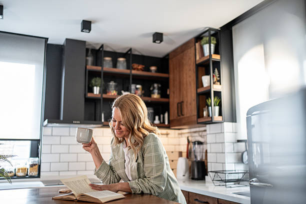 istock Smiling woman reading a book and drinking tea in a modern kitchen 2209401885
