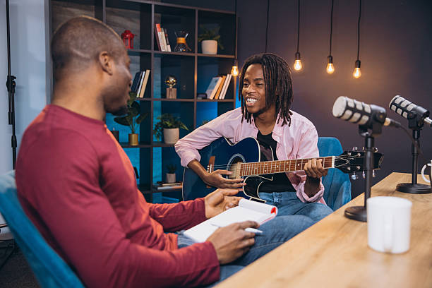 istock Young African American musician playing acoustic guitar while engaging in conversation with a podcaster inside a vibrant recording studio 2209402641