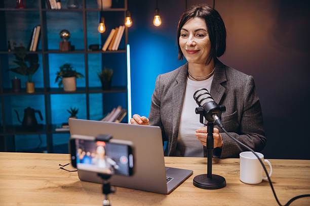 istock Mature podcaster speaking into professional microphone, working on laptop from home recording studio with focused expression 2209402794