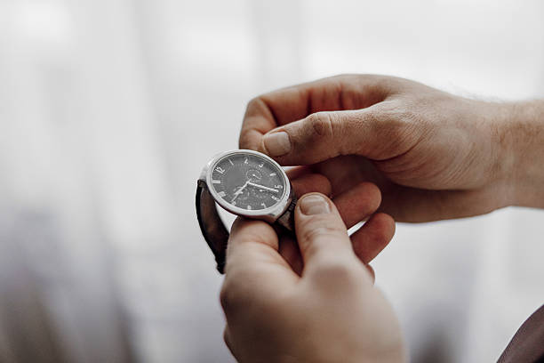 A man is holding a watch in his hand. The watch is black and silver. The man is looking at the watch, possibly checking the time