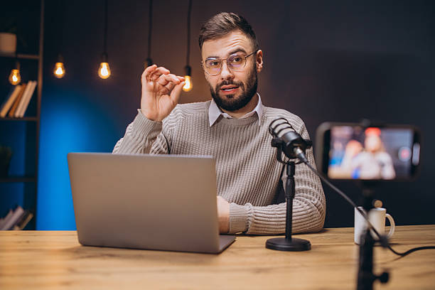 istock Young man recording a podcast using a professional microphone and laptop in a home studio, gesturing while speaking 2209403034