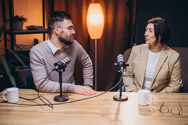 istock Couple talking into microphones during podcast recording, surrounded by professional audio gear in home studio setting 2209403040
