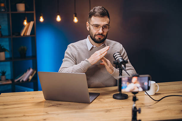 istock Young man gesturing while recording a podcast using professional microphone and laptop in home studio 2209403042