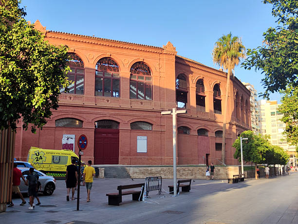 People walking at La Malagueta, a bullring at Málaga, Andalucía, Spain. It is located in the eastern district of Málaga, in its namesake neighbourhood of La Malagueta. The style of the building is Neo-Mudéjar and it takes the form of a 16-sided hexadecagon.