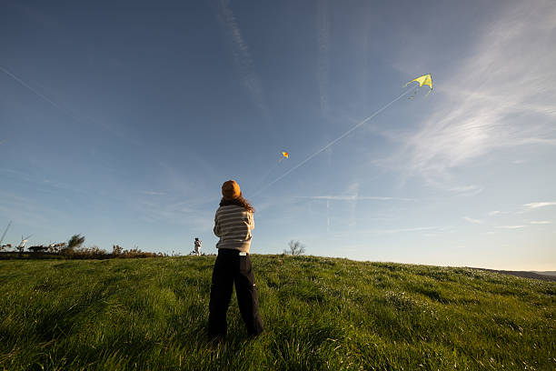 A 9 years old Asian girl flying a kite in the prairie with a background of well-lit sky and grass. Happy childhood life, education. Leisure. Entertainment background.