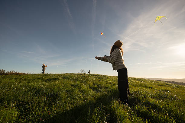 Side View Of Girl Flying Kite Against Orange Sky