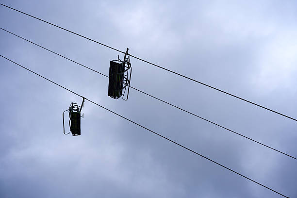 Two chairlifts hang suspended, black silhouettes against a grey sky. Taut cables create abstract geometry, evoking a silent pause.