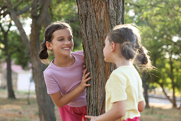Teenage girl and her younger brother have an exciting time playing by a tree in the park, embracing the joys of childhood