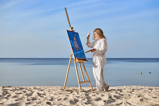 istock Young female artist painting on tranquil beach setting 2209416185