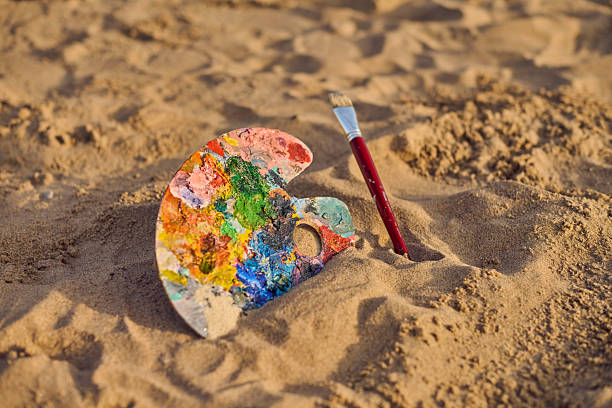 istock Colorful artist palette and brush on sandy beach 2209416211