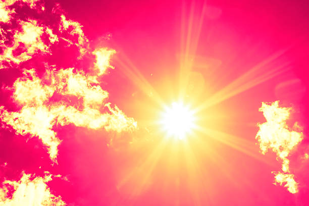 Bright sun with beautiful beams in the sky with some clouds. Toned in red color, space for copy.